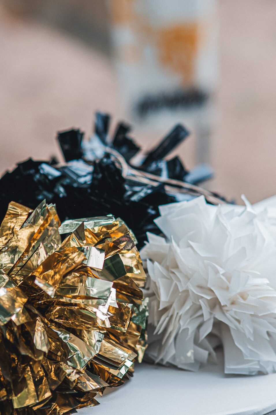 Drei Pompons in Schwarz, Gold und Wei&szlig; liegen nebeneinander auf einem Tisch.