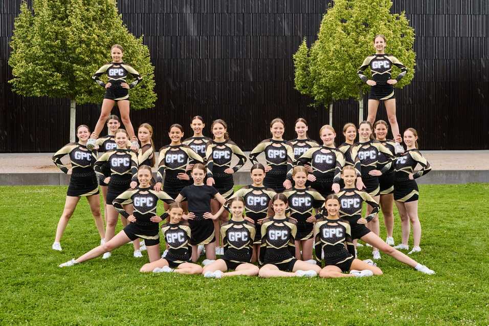 Gruppendynamik von Cheerleaderinnen in einheitlichen Outfits, in Formation auf einer Wiese vor einem modernen Hintergrund.