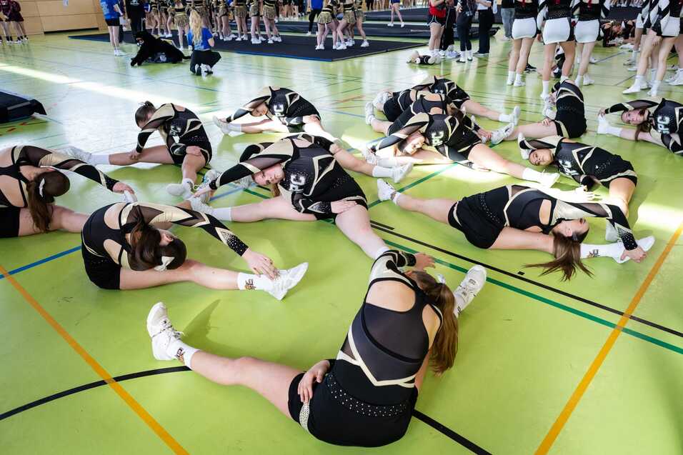 Gruppende Cheerleader dehnen sich auf einer gr&uuml;nen Sportfl&auml;che vor dem Wettkampf, in sportlichen Outfits mit langen &Auml;rmeln.