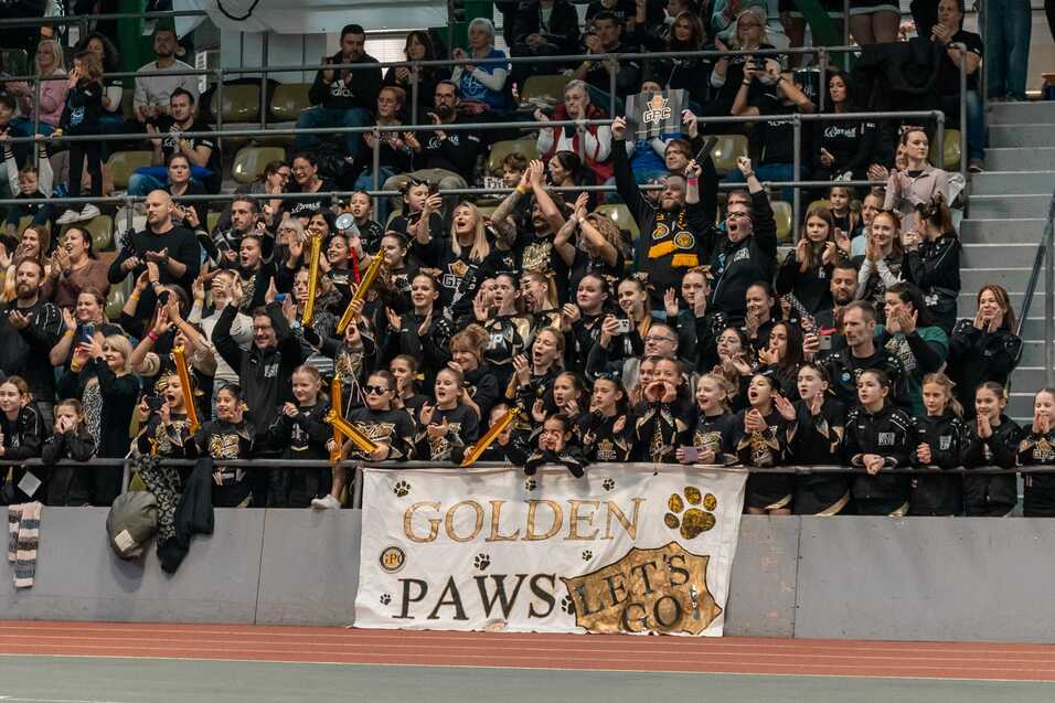 Jubelnde Zuschauer in einheitlicher Kleidung feuern ihre Mannschaft an, umrahmt von einem Transparent mit &bdquo;GOLDEN PAWS&ldquo;.