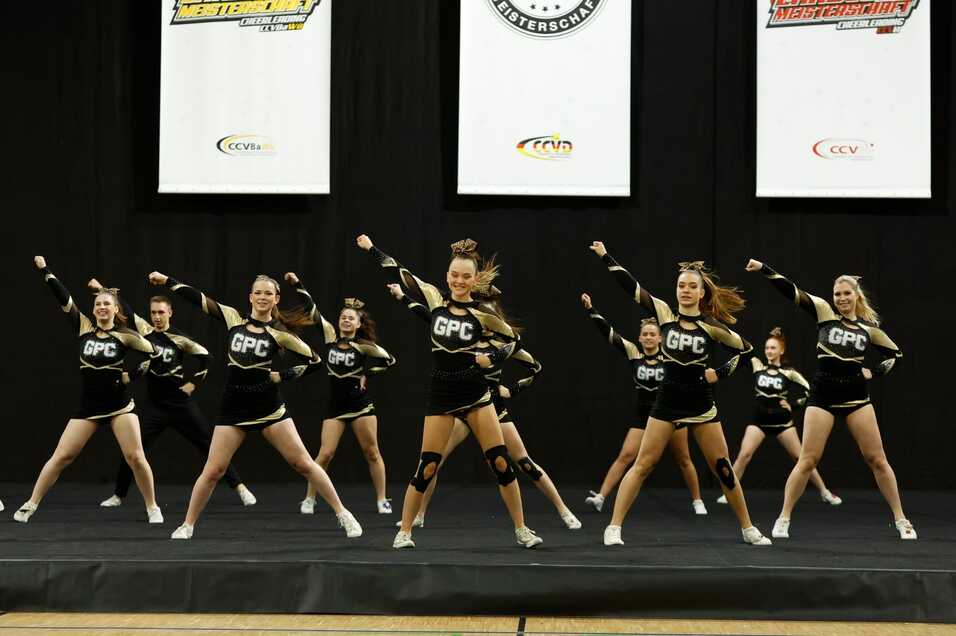 Cheerleader-Gruppe in Schwarz-Gold-Kost&uuml;men f&uuml;hrt eine Choreografie auf einer B&uuml;hne vor.
