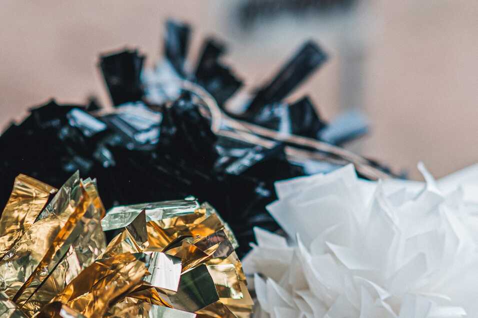 Drei Pompons in Schwarz, Gold und Wei&szlig; liegen nebeneinander auf einem Tisch.